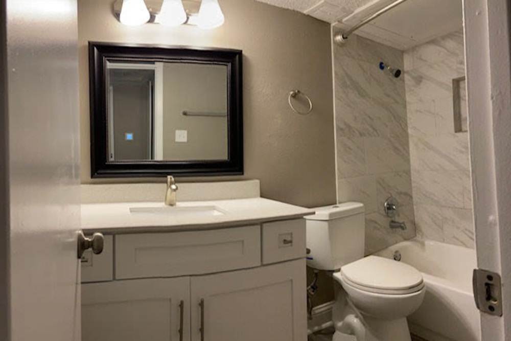 Modern bathroom with vanity light, mirror, sink, commode and standard bathtub at Mission Pointe Club Apartments in Euless, Texas