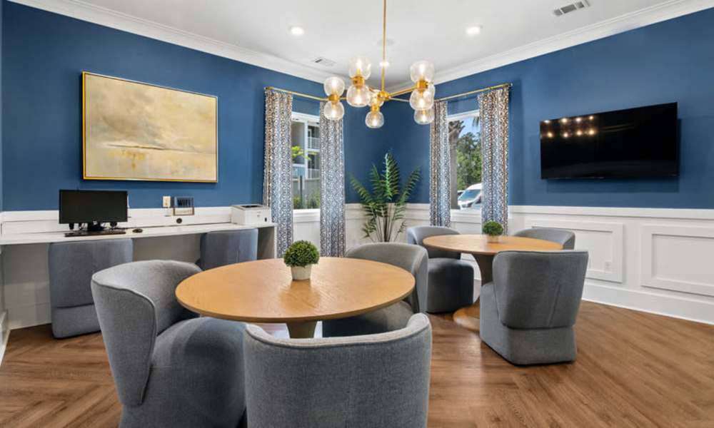 Modern community lounge with wood-style flooring, round tables, and stylish seating under pendant lighting at Everett at Port Wentworth in Port Wentworth, Georgia