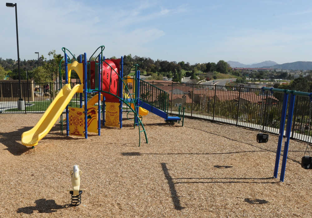 Delightful playground featuring vibrant slides and swings, surrounded by lush landscaping and stunning mountain views, perfect for family fun and outdoor play at Cresta Bella in San Diego, California
