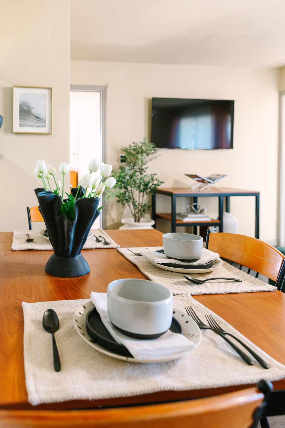 Dining area with wooden table, place settings, and wall-mounted TV in open living space at The Holly in Lubbock, Texas