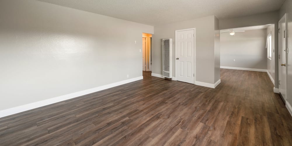 Living room with plenty of space, wood-style flooring, and connecting to kitchen at Garden Court Apartments in Alameda, California