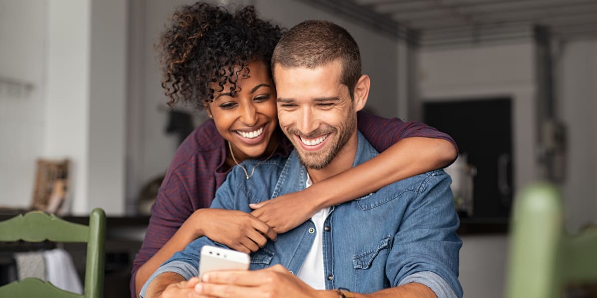 Two smiling residents looking at a phone at One90 Main in Rowlett, Texas