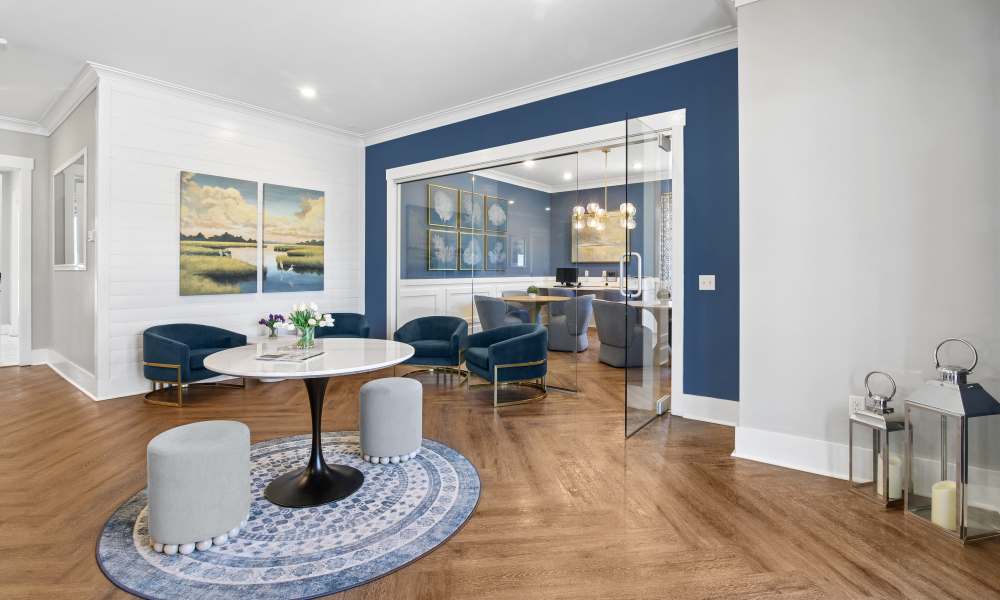 Modern lounge area with wood-style flooring, round table, and blue accent chairs at Everett at Port Wentworth in Port Wentworth, Georgia