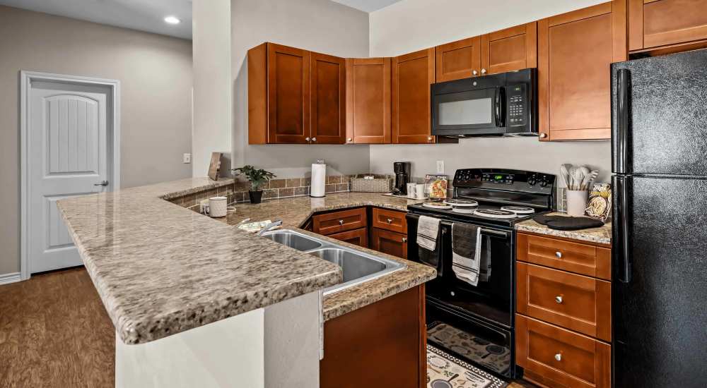 Cozy kitchen with wooden cabinets and black appliances at Stonegate in Hallsville, Texas