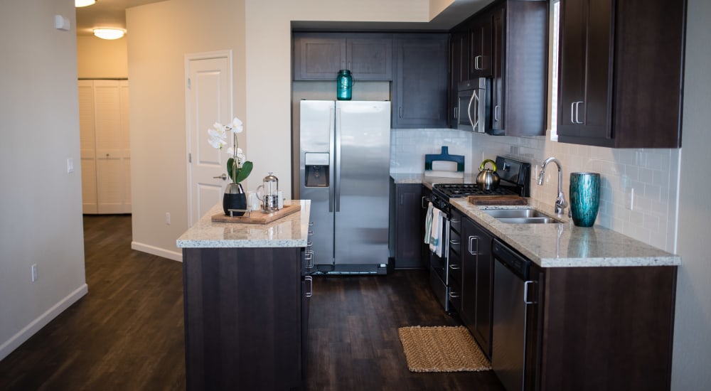 Tracy, California, Luxury Apartments - Aspire - Modern Kitchen with Wood-Style Flooring, Dark Wooden Cabinetry, Stainless Steel Appliances, Kitchen Island, Light Granite Countertops, and White Tile Backsplash