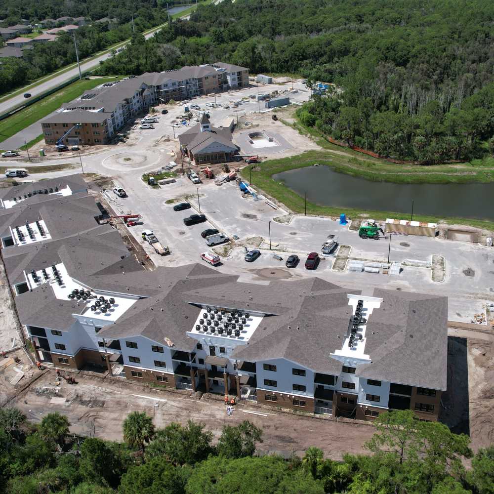 Aerial overview of an apartment community under construction with buildings, parking area, and adjacent pond at The Cove in Port St Lucie, Florida.