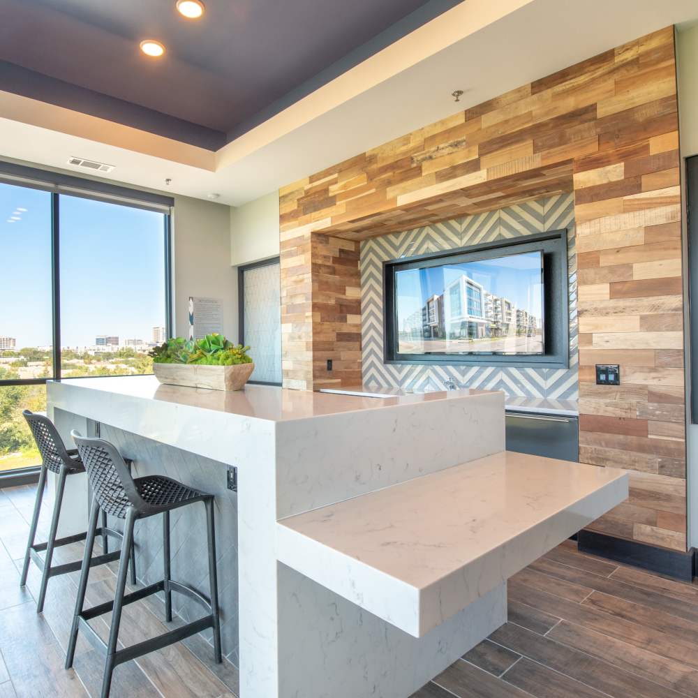 Resident lounge room with large white marble island and two black barstools with floor to ceiling windows at Hall Street Flats in Dallas, Texas