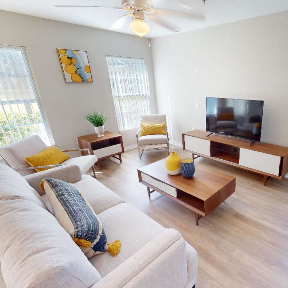 Bright living room with wood-style flooring, modern furniture, and large windows letting in natural light at The Reserve at Brookhaven in Palm Coast, Florida