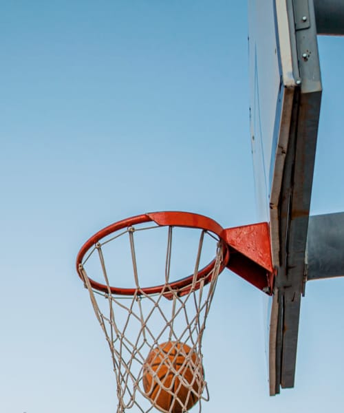 Basketball hoop with a ball approaching the net against a clear blue sky at Portland School in Portland, Michigan