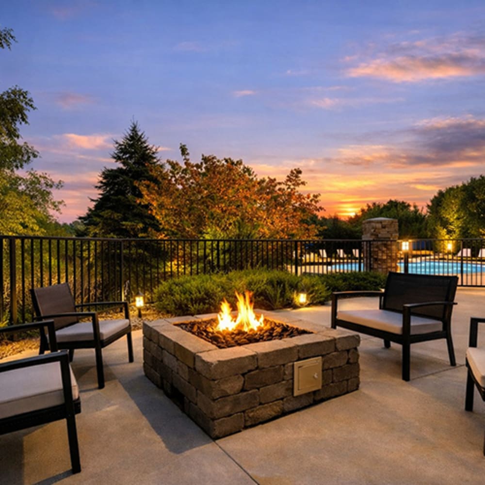 Cozy outdoor fire pit surrounded by seating, with a sparkling pool in the background at sunset at 43 North Apartments in Grand Haven, Michigan