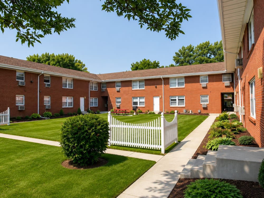 Lush green lawn with white picket fence and red brick apartment buildings at South Oak in Ames, Iowa