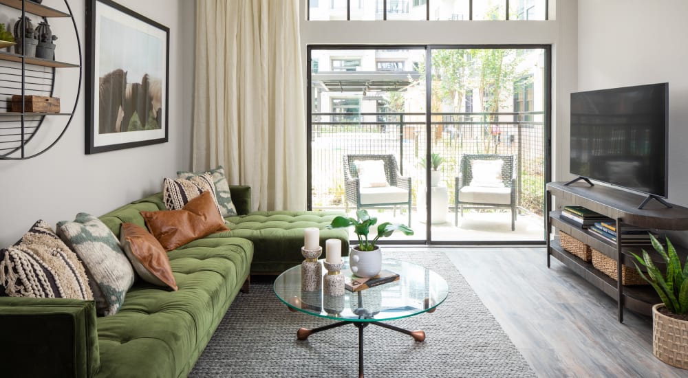 Furnished living room with green sofa and large sliding glass door to balcony at Bellrock Sawyer Yards in Houston, Texas