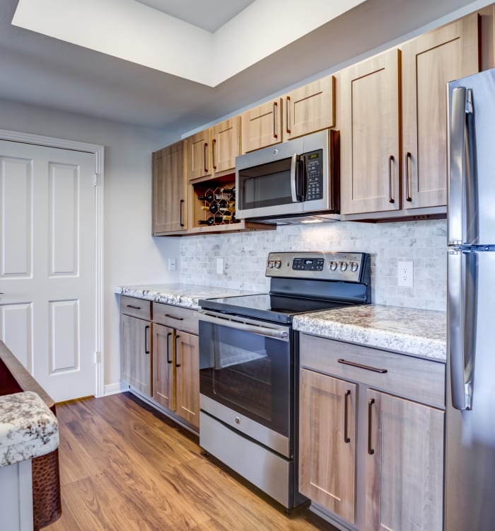 Granite countertops, stainless-steel appliances, and gorgeous wood cabinets and floor in model home kitchen at Riata Austin in Austin, TX