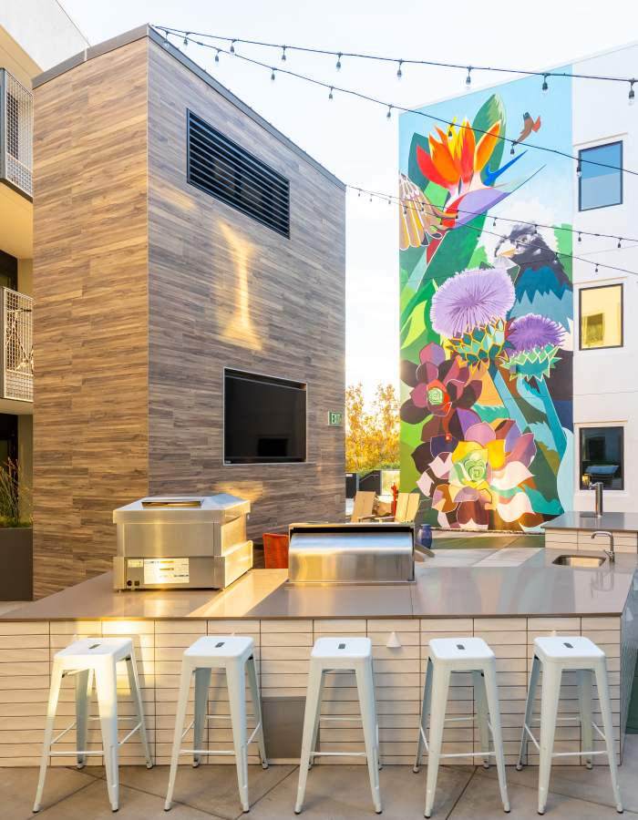 Outdoor kitchen with stainless steel appliances, bar stools, and colorful mural backdrop at Exhibit at J Town in San Jose, California