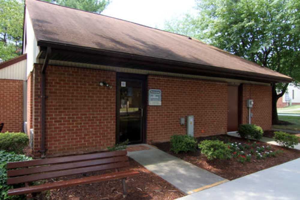 Exterior brick building entrance with wooden bench, shrubs and green landscaping at Shenandoah Apartments in Winchester, Virginia