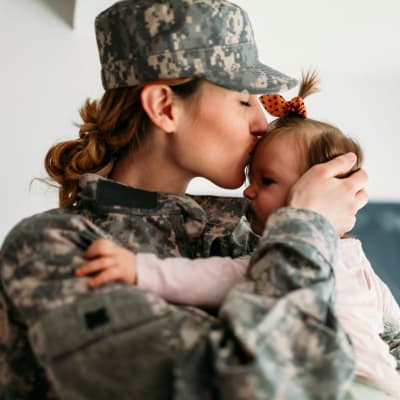 A mother in uniform kissing her daughter on the head at Del Mar II in Oceanside, California