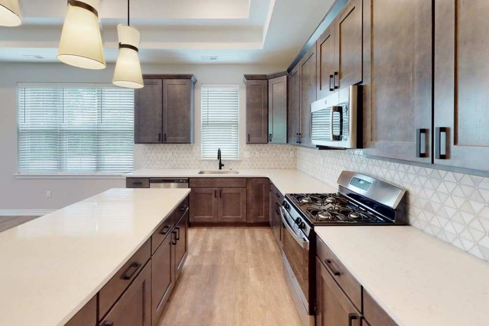 Bright kitchen with island, gas range, microwave, tiled backsplash, dark cabinets, and window blinds at Encore at West Valley in White Lake, Michigan