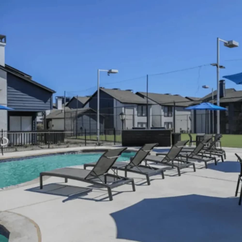 Resort-style pool with lounge chairs and umbrellas at The Larsen Apartments in Dallas, Texas