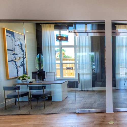 Modern office space with glass doors, large windows, and natural light filtering through sheer curtains at The Mezzanine at Freedom in Charlotte, North Carolina