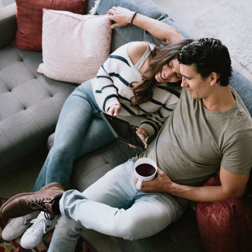 Residents browsing a tablet and drinking coffee on a couch in a home at Bayview Hills in San Diego, California