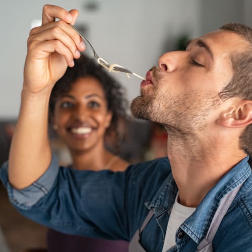 A man tasting noodles while a woman smiles in the background at Brookside Heights Apartments in Cumming, Georgia