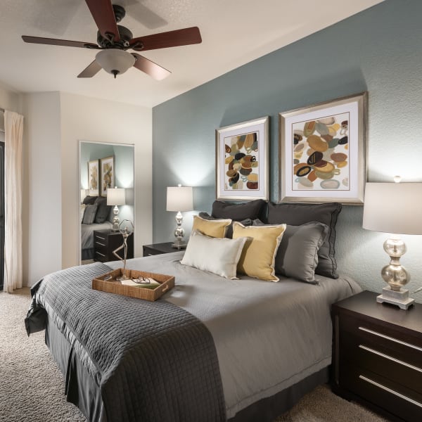 Well-decorated master bedroom with ceiling fan and sliding door to private balcony of model home at San Prado in Glendale, Arizona