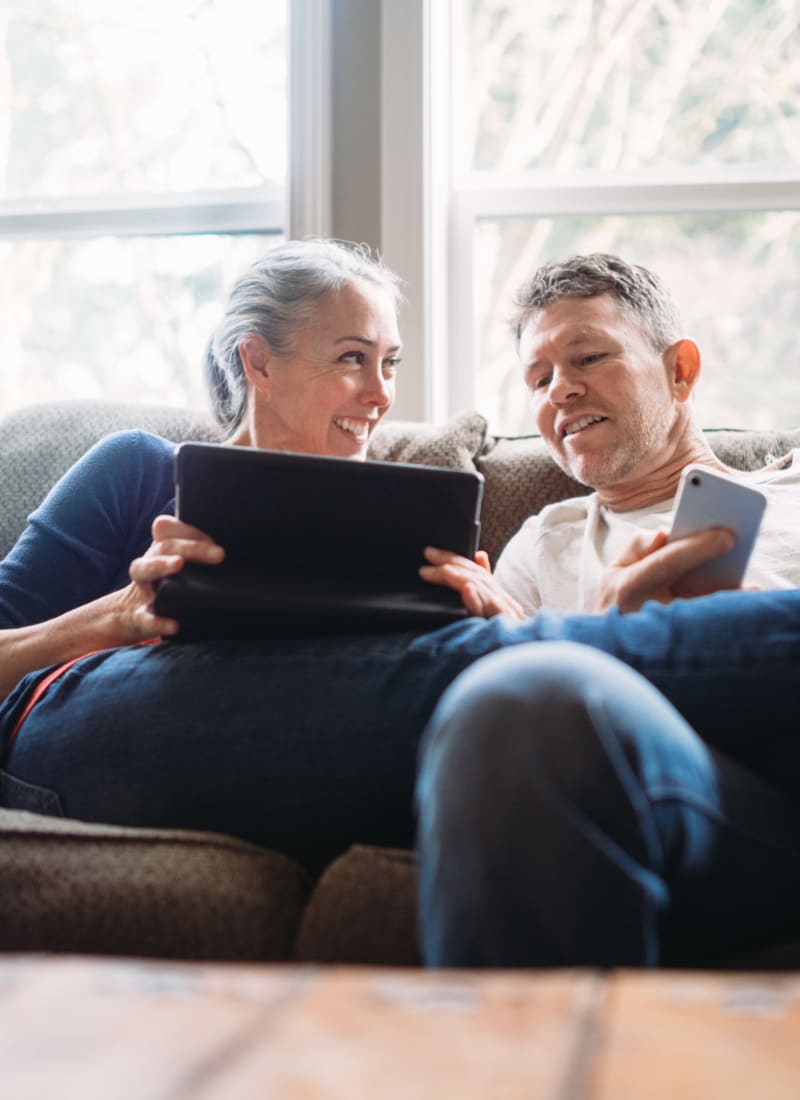 Residents relaxing on couch with tablet and smartphone at Marquis Bandera in San Antonio, Texas
