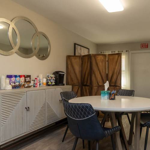 Bright community dining area with round table, modern chairs, and decorative mirrors on walls at Pleasant View Apartments in Charlotte, North Carolina