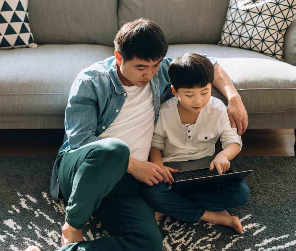 Resident father helping his son do schoolwork on a laptop in their new home at Sofi at Cedar Mill in Portland, Oregon