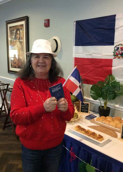 Resident posing for a photo in front of international dishes at a passport dining event at Grand Villa of Port Charlotte in Port Charlotte, Florida