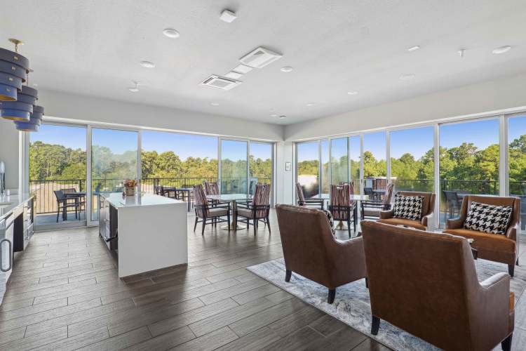 Bright lounge at Reserve Woodland Lakes with large windows, leather chairs, island counter, and dining tables.