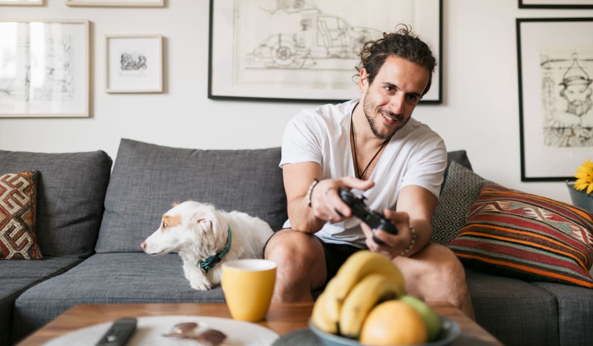 A resident playing video games with his dog on the couch next to him at Clearleaf Crossing in Bryan, Texas