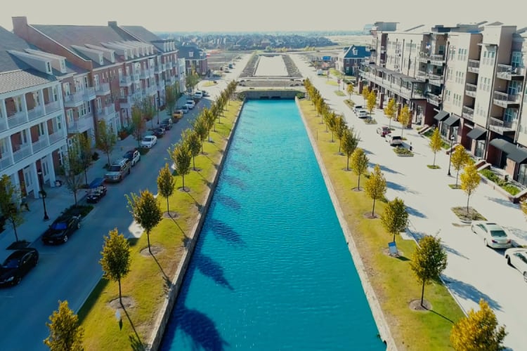 Walkway between apartment buildings with a serene water feature running through the center, creating a peaceful and scenic environment at Watermere at Frisco in Frisco, Texas.