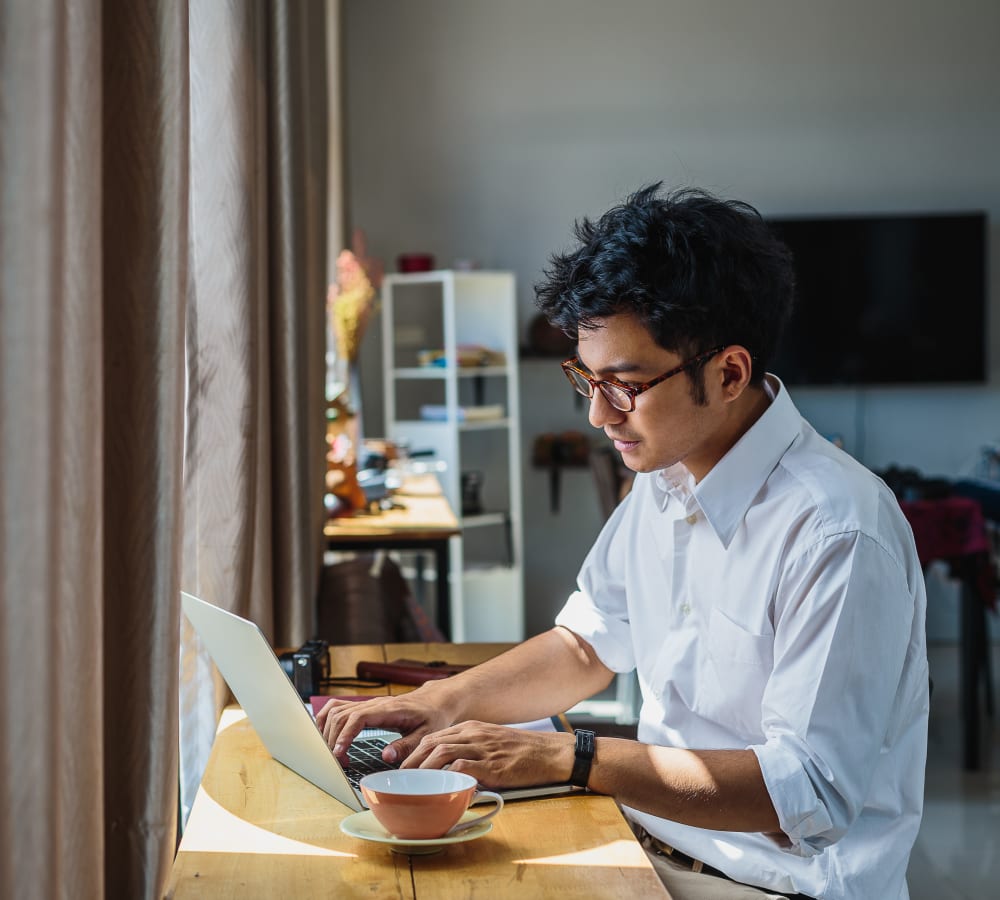 A man sitting at a table using his laptop in an apartment at Stonecreek Club in Germantown, Maryland