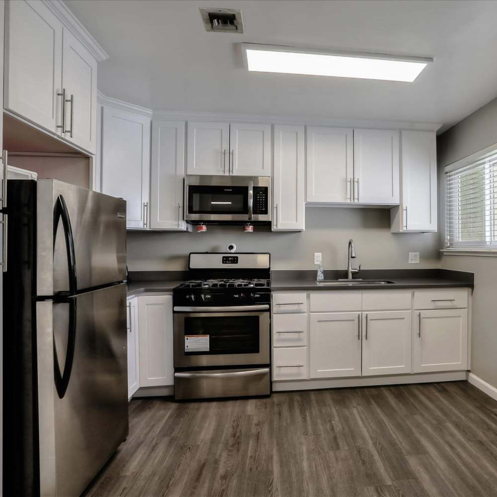 Kitchen with stainless stell appliances, white wood cabinet and wood-style flooring at Santa Teresa Apartments in San Jose, California
