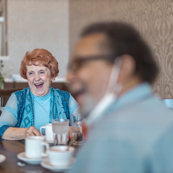 Two residents laughing while talking over coffee at The Madison Senior Living in Kansas City, Missouri