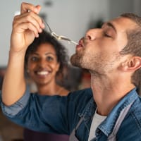 A man tasting the food he's making with a smiling woman in the background at EOS in Orlando, Florida