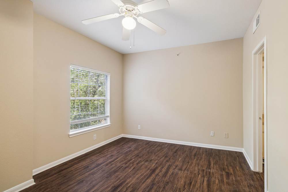 Unfurnished bedroom with ceiling fan, wood-style flooring and large windows at Bristol Apartments in Houston, Texas