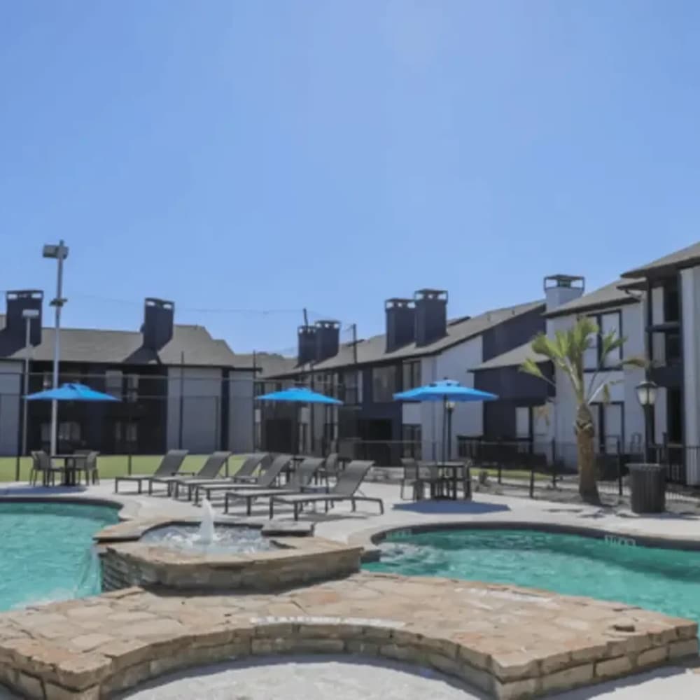 Resort-style pool with lounge chairs and umbrellas at The Larsen Apartments in Dallas, Texas