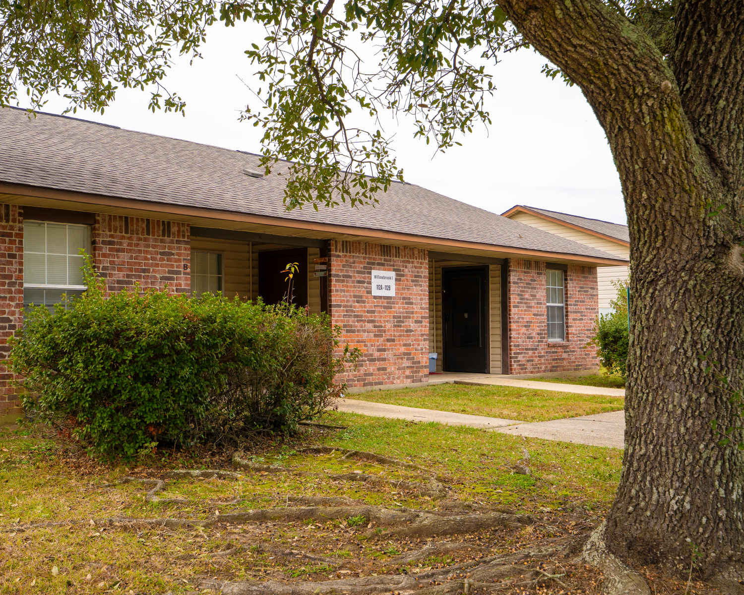Brick apartment building with landscaped bushes and tree in front, welcoming entrance and pathways at Willowbrook I in Lafayette, Louisiana