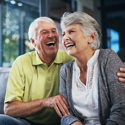 Resident couple sitting on the couch laughing at Deephaven Woods in Deephaven, Minnesota