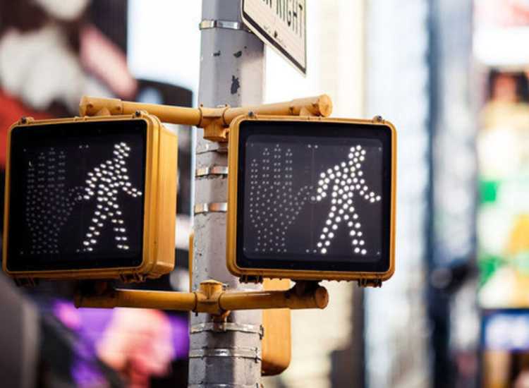 A traffic light with a pedestrian crossing sign, located near a busy commuting point at Broadway Street Apartments in Lowell, Massachusetts