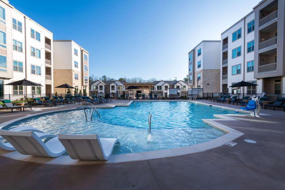 Large outdoor swimming pool area surrounded by apartment buildings under a clear blue sky at The Reserve at Patterson Place in Durham, North Carolina