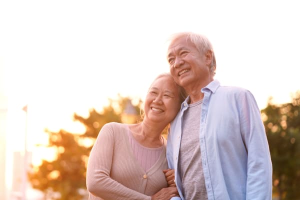 Asian senior couple hugging and smiling at something in the distance