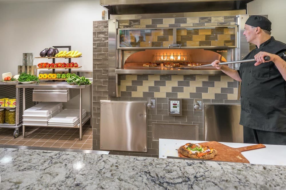 Chef artful removes flatbread from oven for enjoyment of residents at The Springs at Greer Gardens in Eugene, Oregon