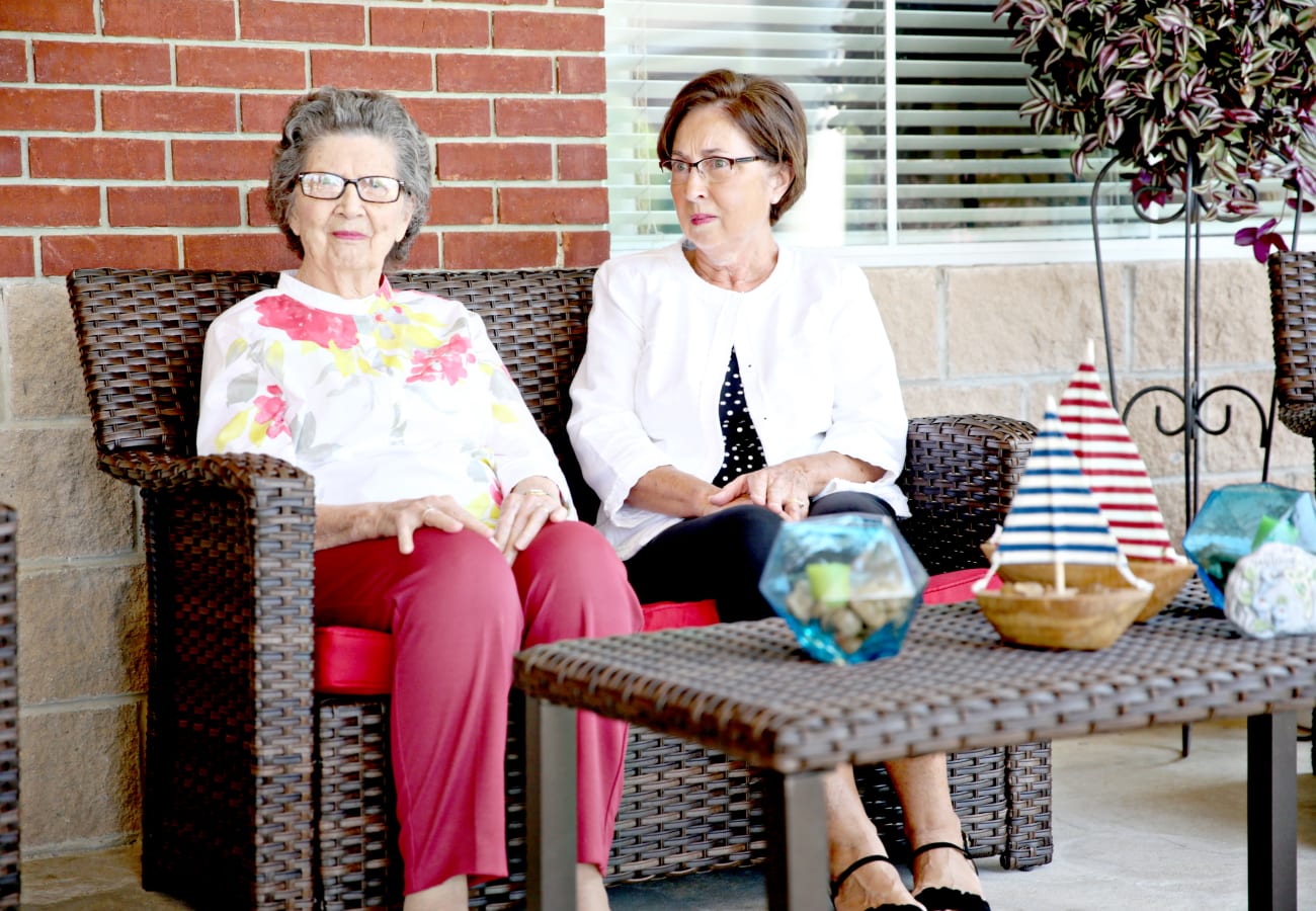 Two women sitting on an outside patio in outdoor furniture at Providence Assisted Living in Searcy, Arkansas