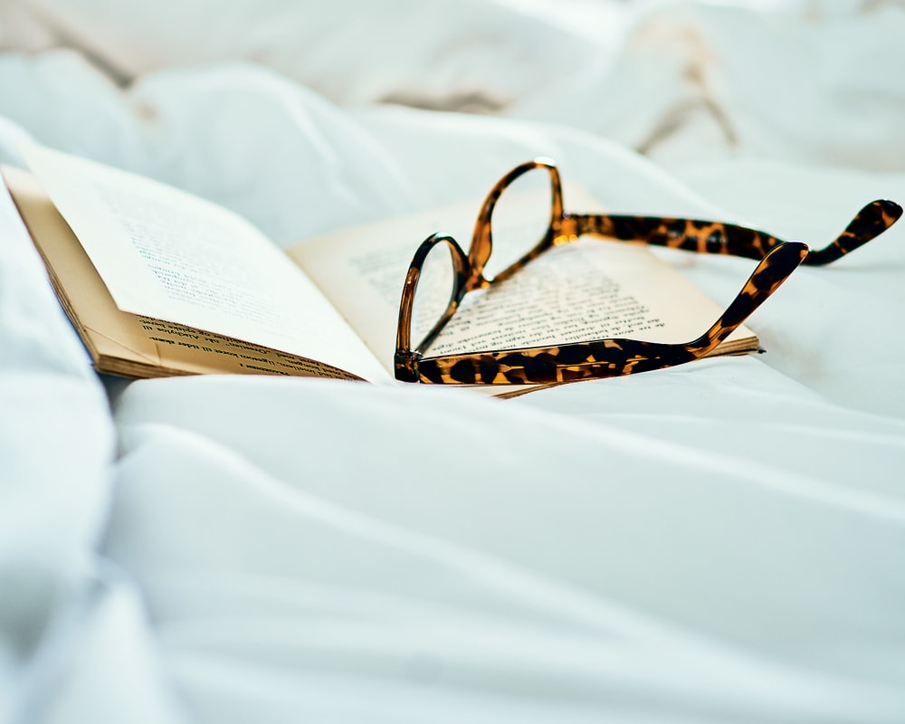 A book and reading glasses sitting on a bed at Edencrest at Tuscany in Altoona, Iowa.