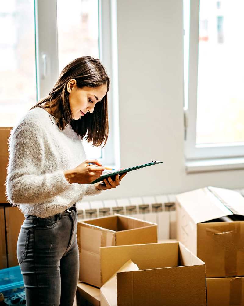 Woman organizing boxes while taking notes in a bright, spacious room with large windows at CSI Mini Storage Alameda in Alameda, California 