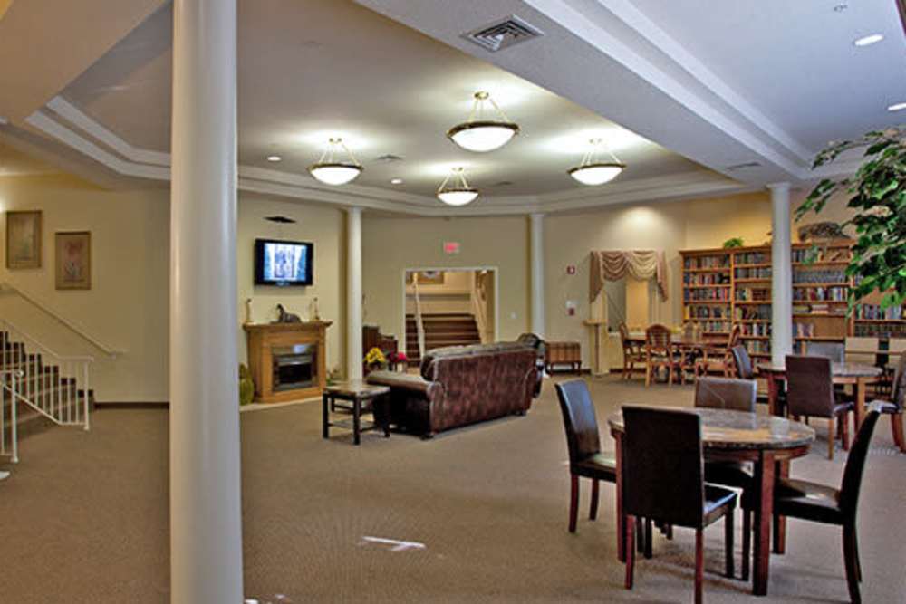 Spacious community lounge with comfortable seating, dining tables, and bookshelves. Warm lighting and inviting atmosphere at Evergreen Senior Community in Bowie, Maryland