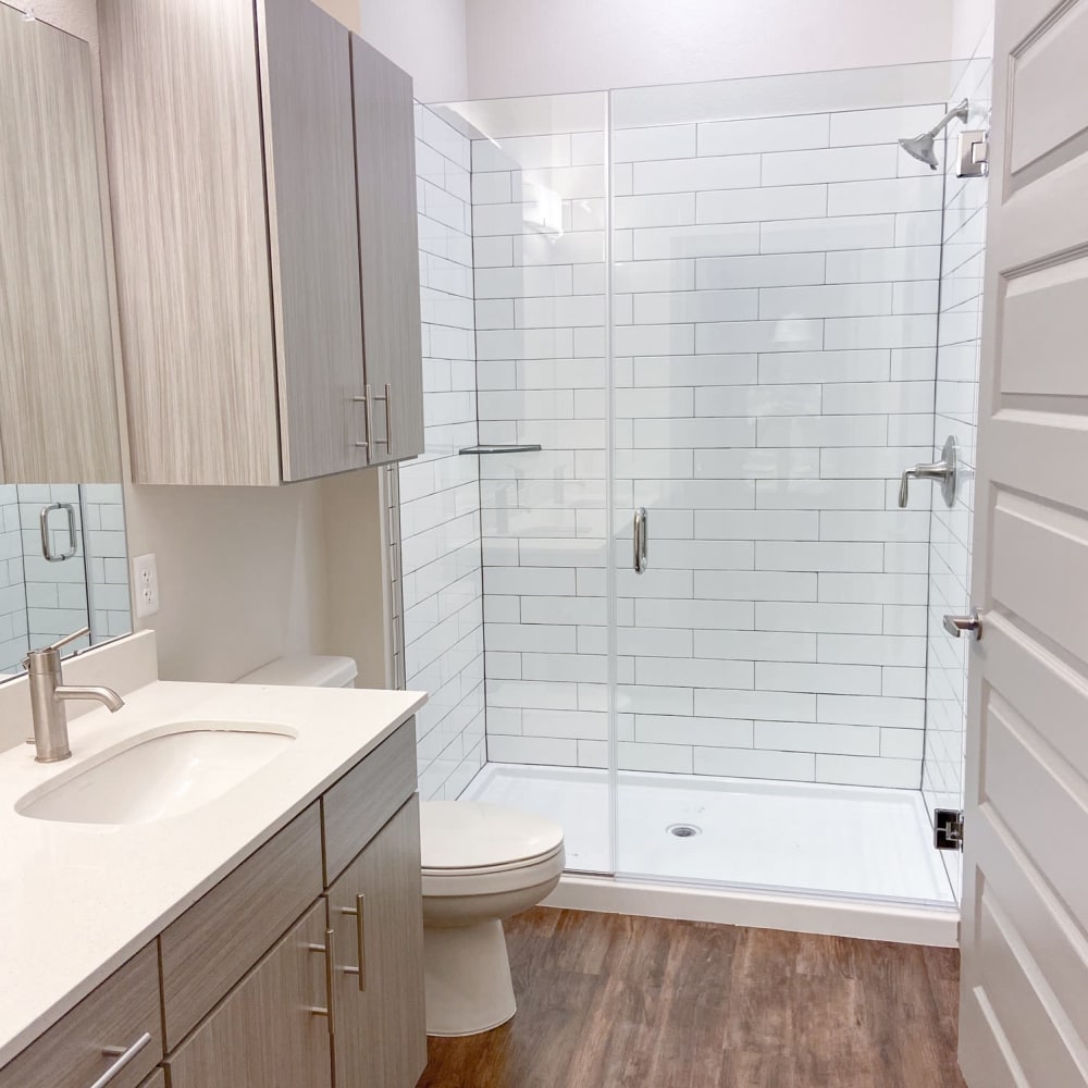 Bathroom with walk in shower featuring white tile, glass door and dark wood patterned floor at The Alcott in Denver, Colorado